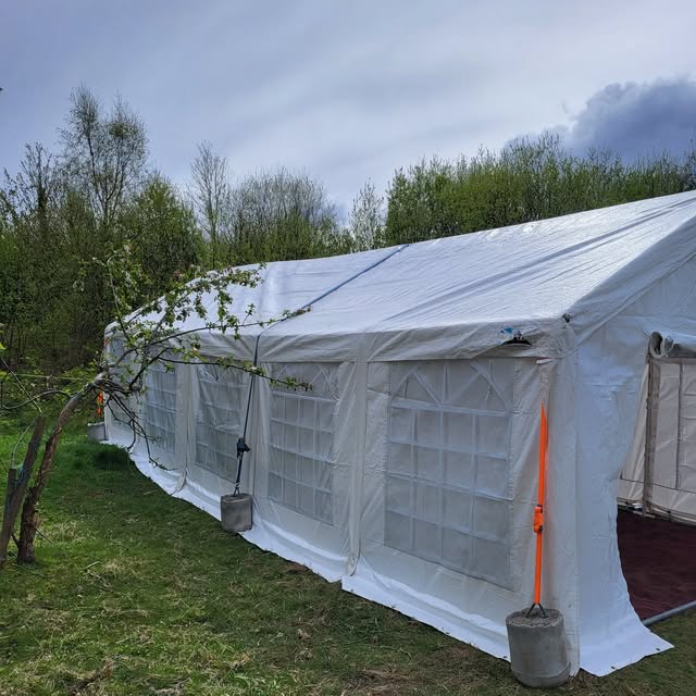 Long white marquee with windowed sides set up in a garden.