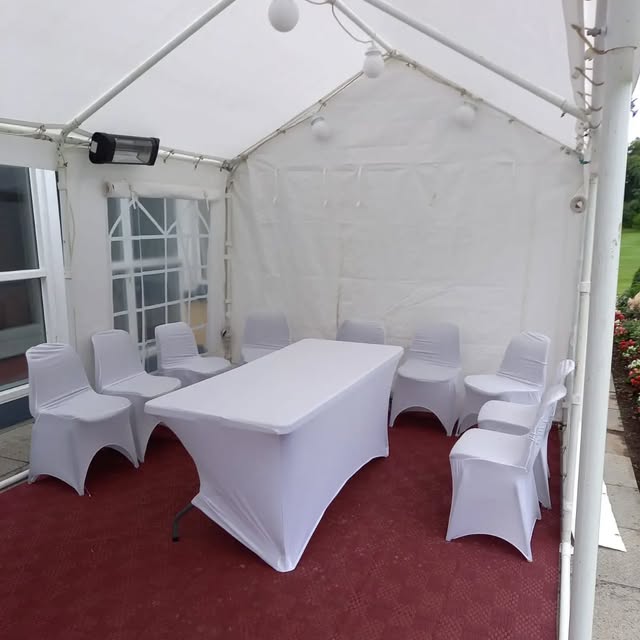 White marquee interior with a rectangular table and fitted white chair covers.
