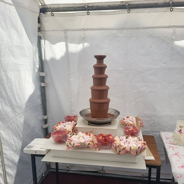 Chocolate fountain surrounded by bowls and trays of sweets inside a marquee.