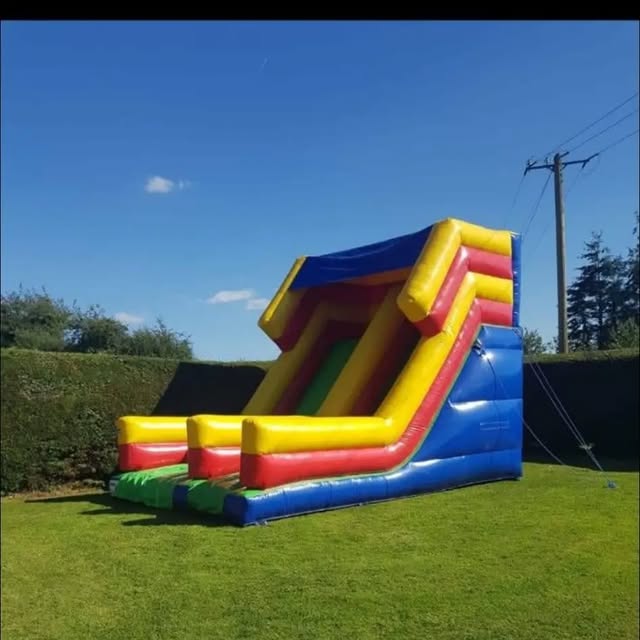 Tall blue, red, yellow, and green inflatable slide on grass.